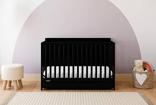 Modern nursery with black crib, stool, and teddy bear in a basket.